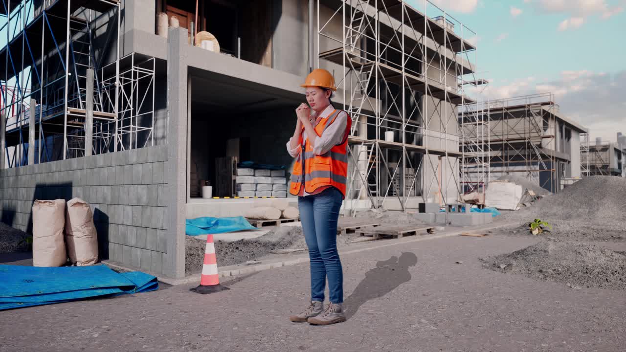 Full Body Side View Of Asian Female Engineer With Safety Helmet Pray For Something While Standing At Construction Site in Progress to New House