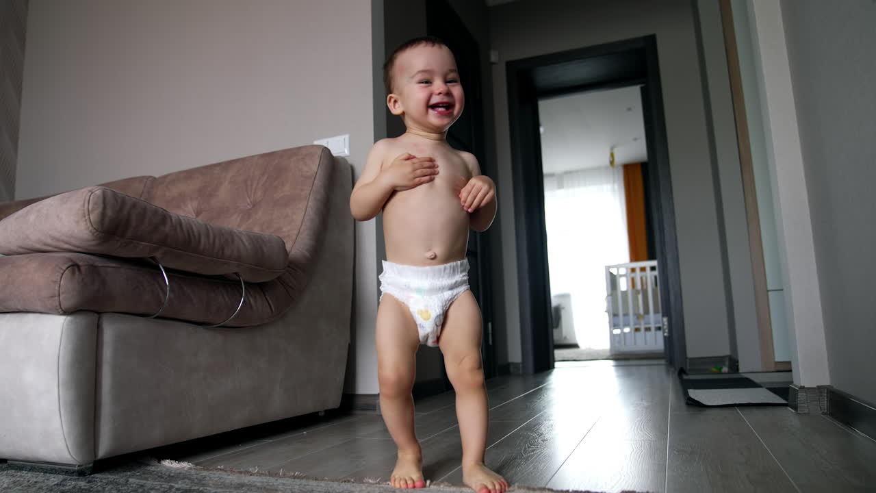 Cute happy Caucasian boy running about the house. Baby in diaper playing at home. Low angle view.