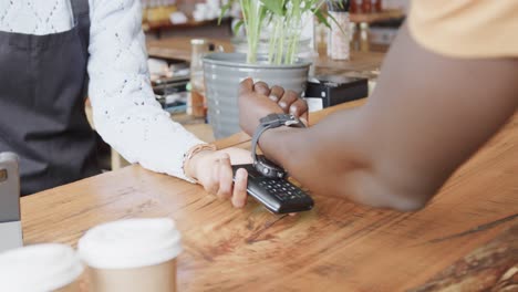 Midsection-of-african-american-man-paying-with-smartwatch-at-coffee-shop,-slow-motion