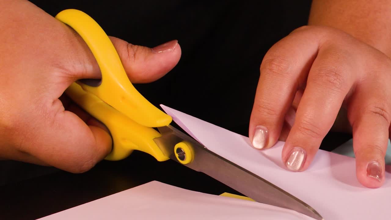 Una ripresa ravvicinata dettagliata di mani che tagliano con precisione carta rosa con forbici giallo brillante