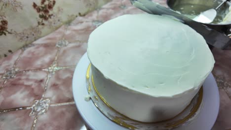 a hand applies a layer of frosting to the cake