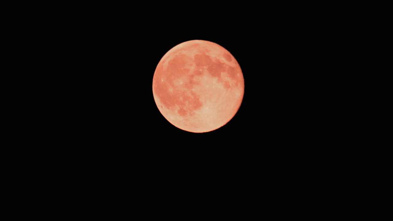 A detailed close up of a full orange moon glowing brightly against a black night sky