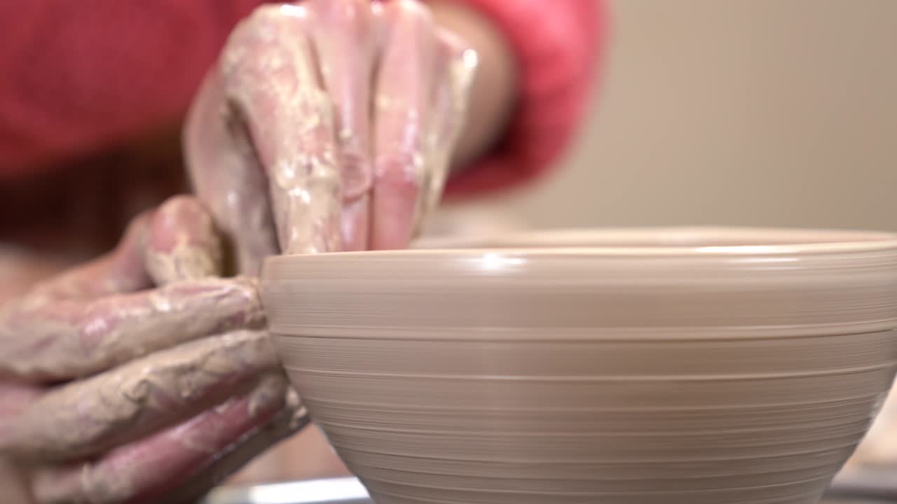 Closeup side view of a muddy hands shaping a clayware on the spinning potter's wheel.