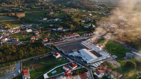 aerial - industrial factory releasing smoke in a rural landscape at sunset