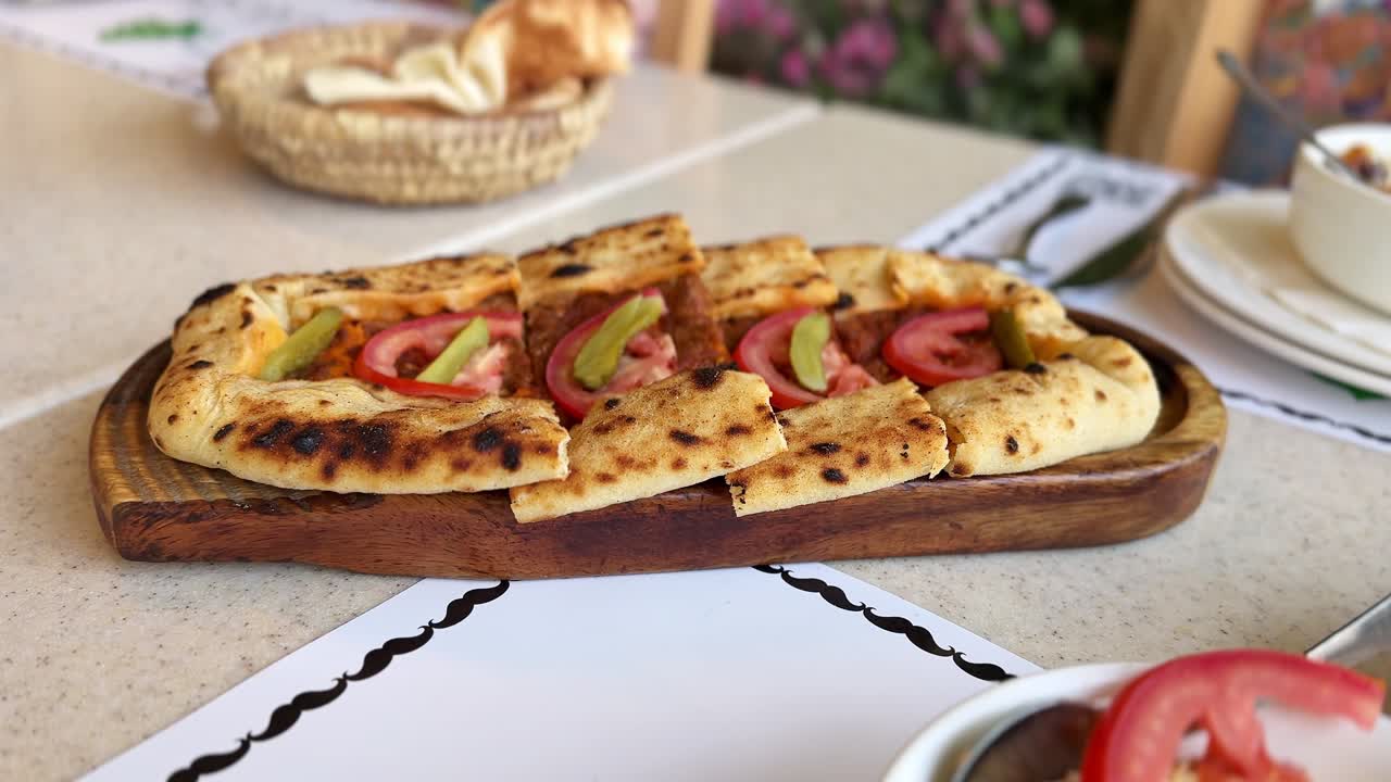 Primo piano di focaccia ovale ripiena su tagliere di legno con ripieno tritato, fette di pomodoro e sottaceti, servita su un tavolo di un ristorante alla luce del giorno