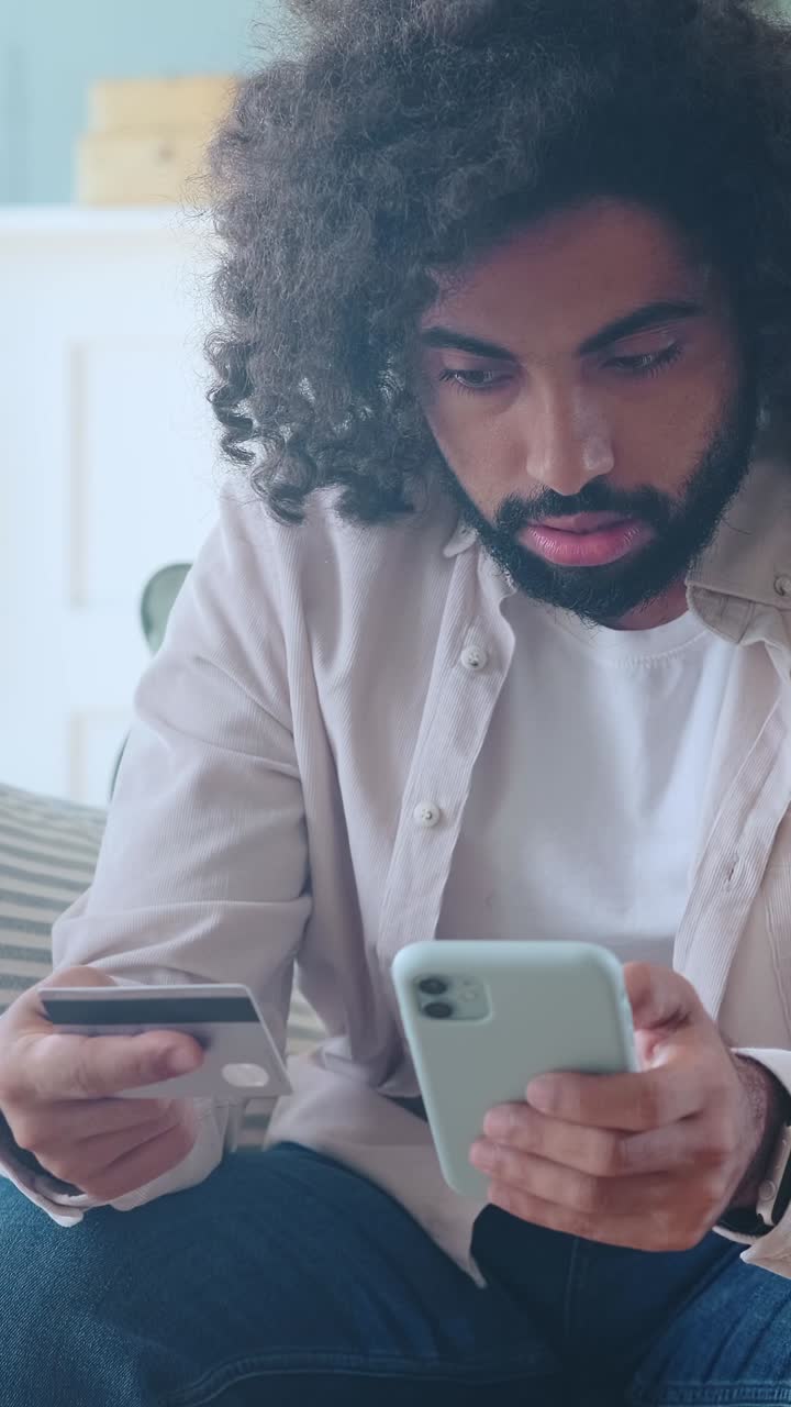 Uomo che controlla il telefono mentre tiene una carta di credito in un accogliente salotto