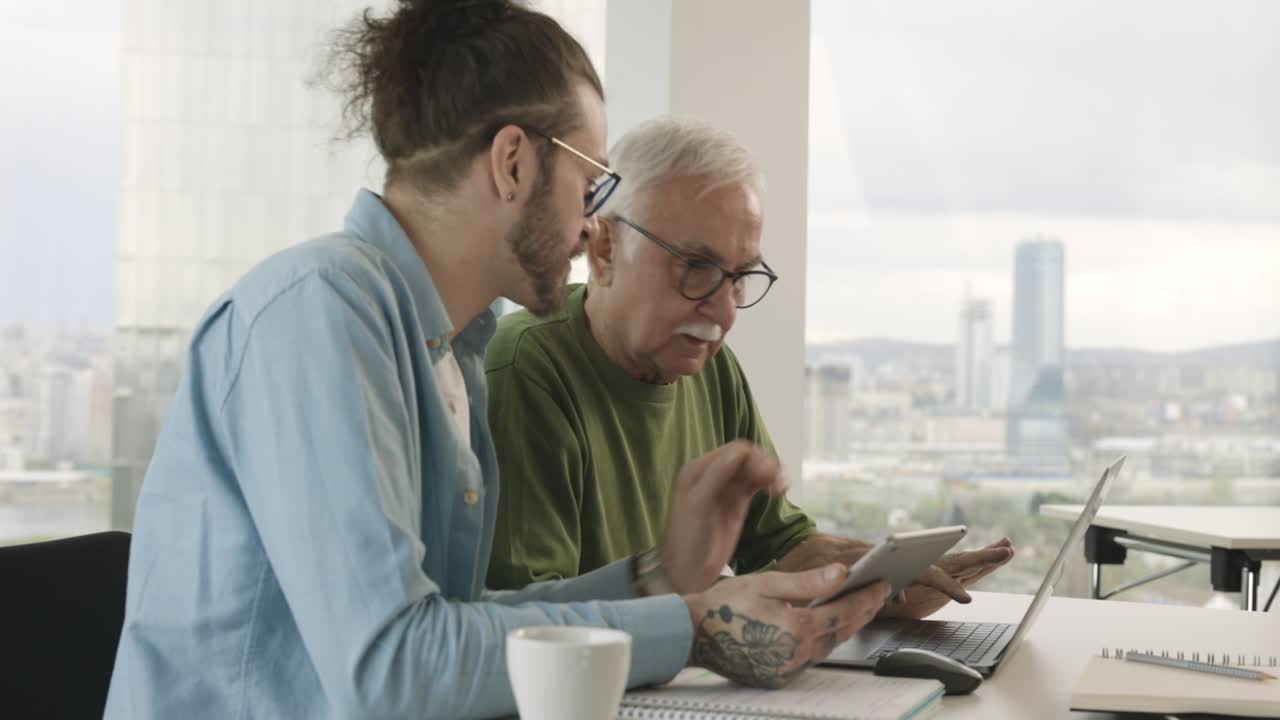 A young hipster educator is teaching a senior male student how to design a website in the classroom.