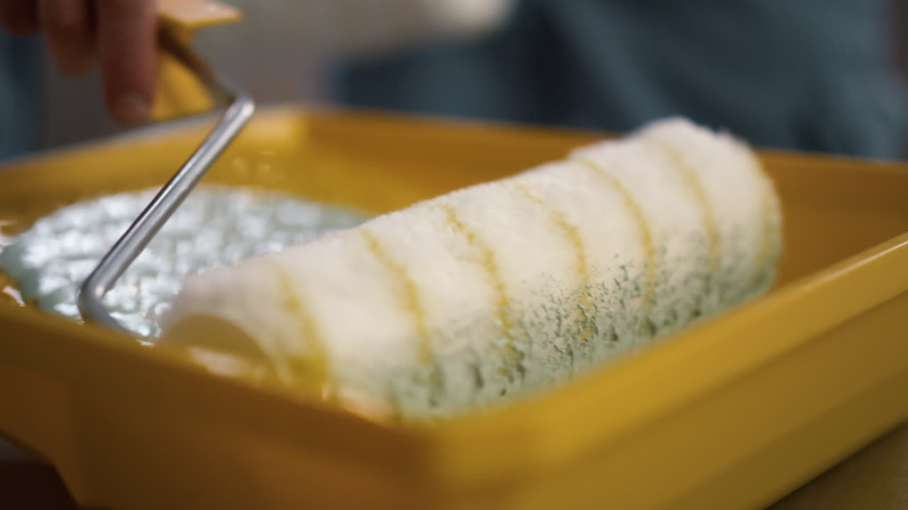 hombre poniendo a mano el rodillo de pintura en la bandeja en el nuevo apartamento.