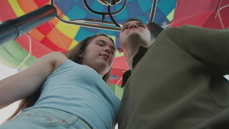 low angle view of romantic couple standing closely and sharing kiss inside vibrant multicolored hot air balloon during scenic flight, expressing affection and connection
