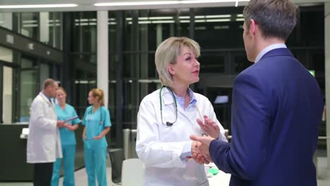 Female-doctor-shaking-hands-with-businessman-in-corridor