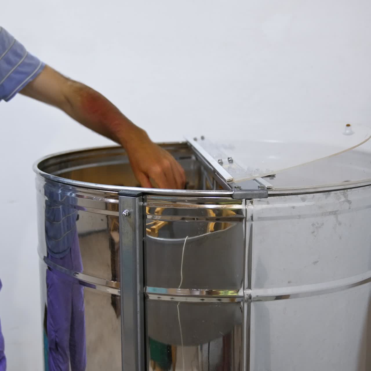 Bee farmer puts the frames into a metal barrel to get honey. Man carefully places the honeycombs into special apparatus