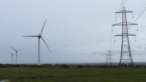 Toma-De-Turbinas-Eólicas-Creando-Energía-Renovable-Justo-Al-Lado-De-Torres-De-Electricidad-Y-Líneas-Eléctricas,-4k