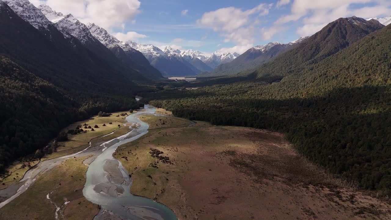 Vista aerea cinematografica con drone di un fiume che serpeggia attraverso una valle sulla strada per Milford Sound. Maestose montagne innevate incorniciano il paesaggio. Nuova Zelanda