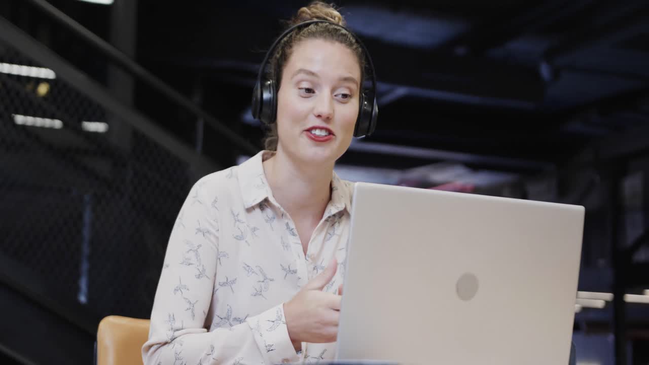 Happy caucasian casual businesswoman making video call using laptop in office lounge, slow motion