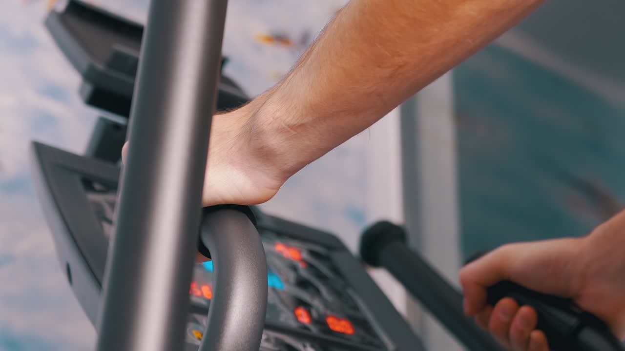 el atleta entrena en un entrenador elíptico en casa, observando el ritmo cardíaco en el monitor