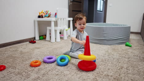 sweet baby boy sitting on the soft carpet plays with pyramid. happy child having fun at home.