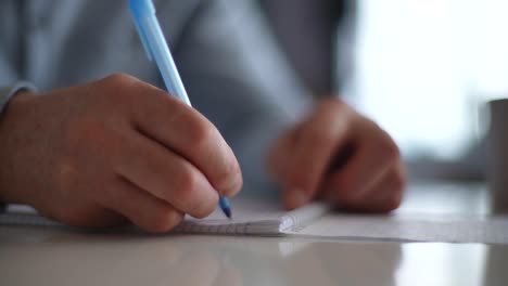 close-up hands of unrecognizable mature adult man writing making notes in organizer book, keep personal diary sitting at table near window.