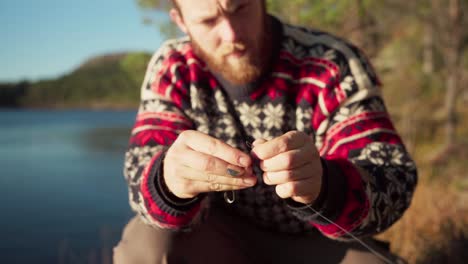 pescador sujetando un gancho a la línea de pesca en la orilla de hildremsvatnet en noruega