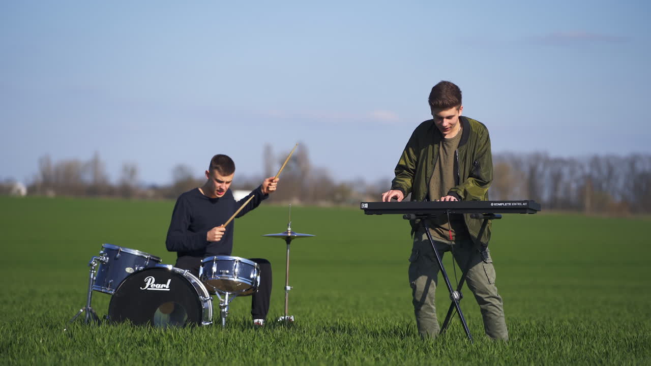 Guys playing musical instruments in the beautiful green plantations. Drummer and piano musician performing in the blurred nature backdrop.