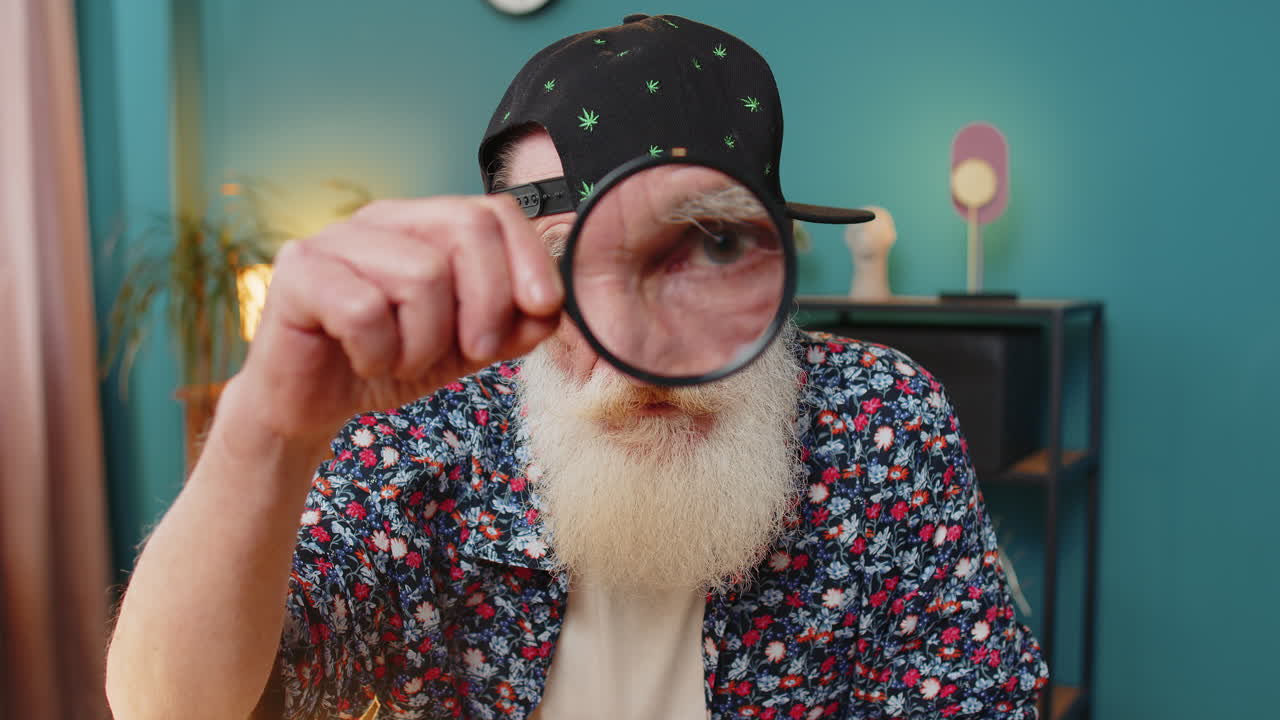 Investigator researcher scientist senior man working at home holding magnifying glass near face