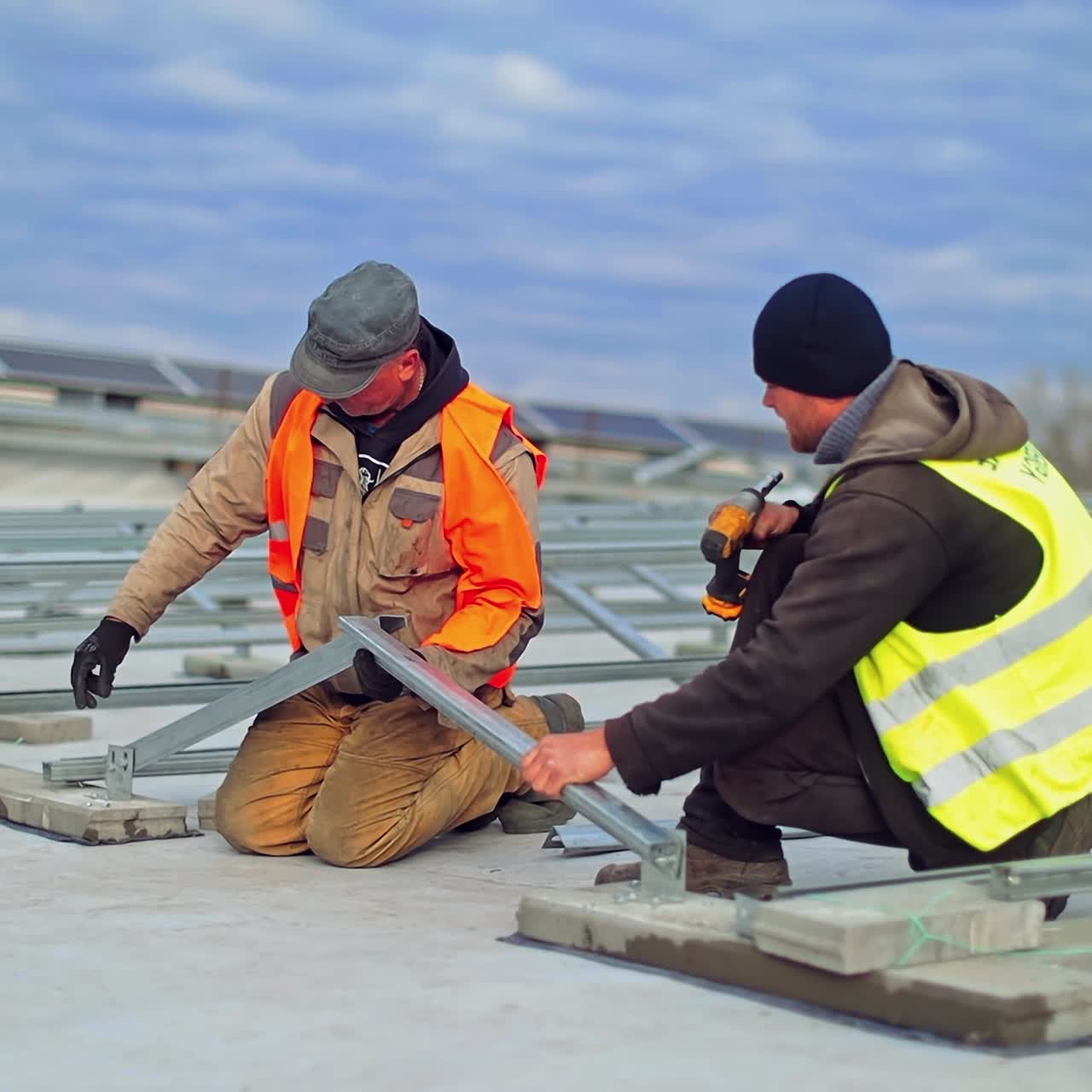 Works to construct solar panels. Two workers installing metal basis for sunny batteries on a flat roof of a huge building. Slow motion.