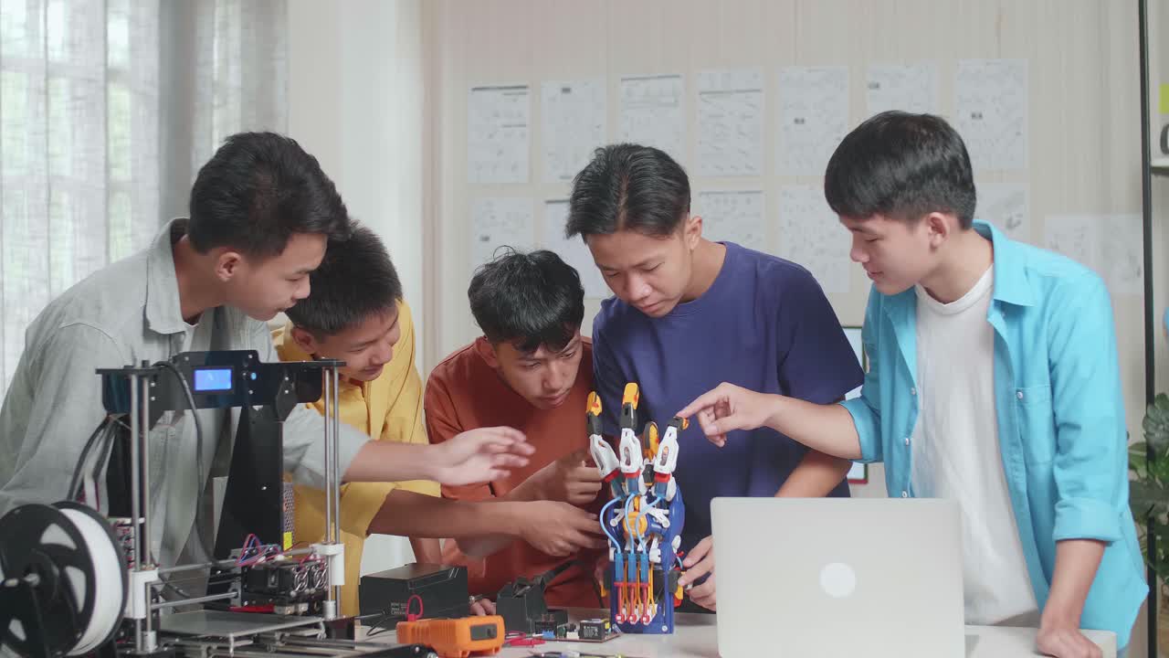 노트북과 3d 프린팅을 가진 젊은 아시아 소년 그룹이 집에서 사이보그 손에 대해 논의하는 동안 미소 짓고 카메라에 팔을 고 있습니다.