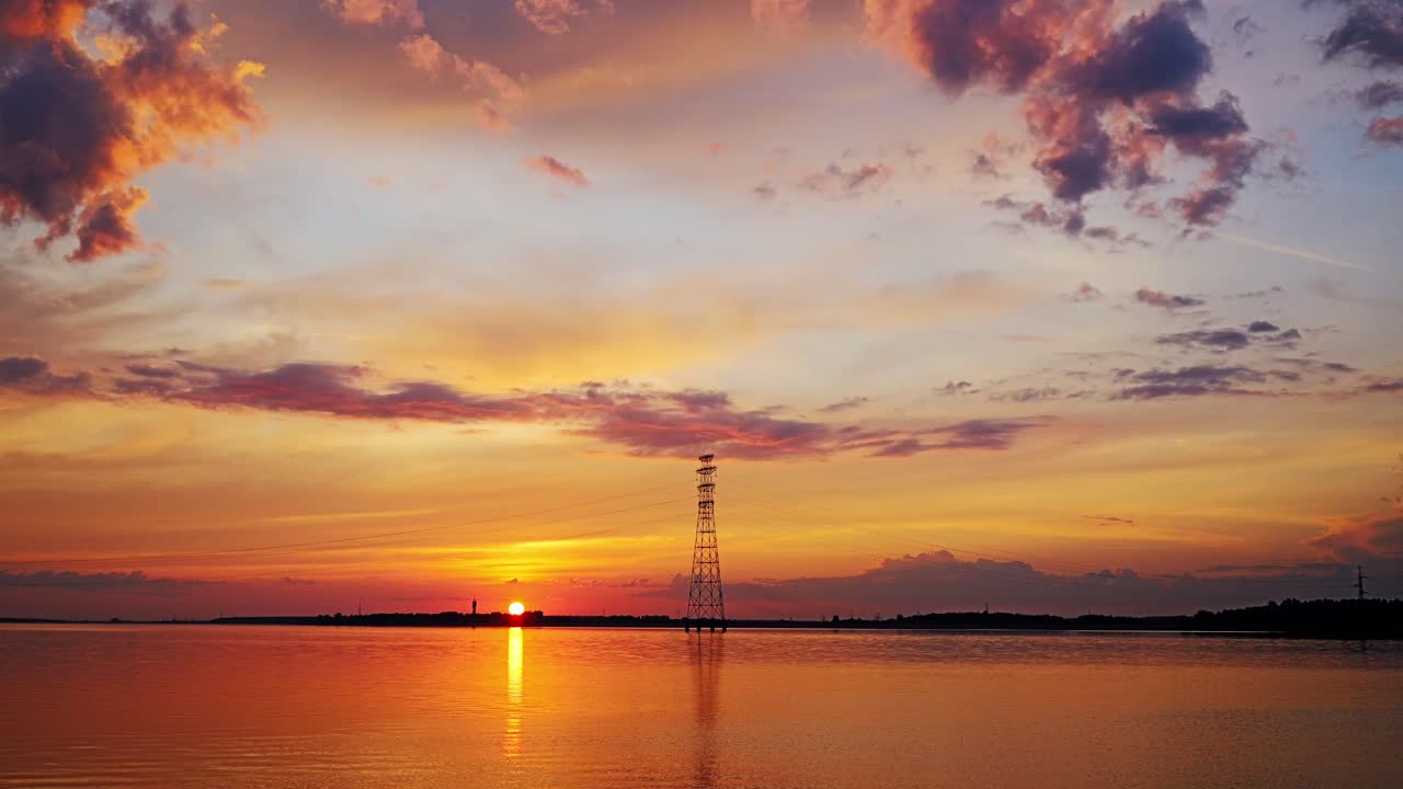 Timelapse sunset paints vibrant clouds above reflective reservoir in Latvia