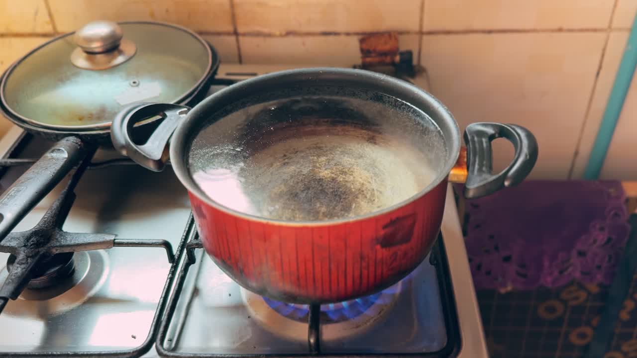Close-up of pot boiling on a gas stove with blue flame and steam in a tiled home kitchen—ideal for cooking, food prep, energy use, and kitchen safety concepts
