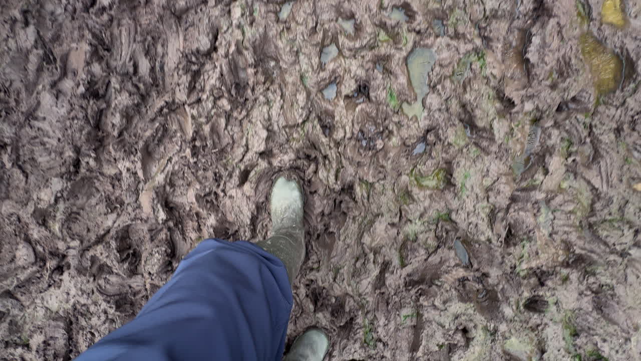 Looking down at the feet of a man wearing wellington boots walking through extreme wet mud after a winter rain storm, Warwickshire, England