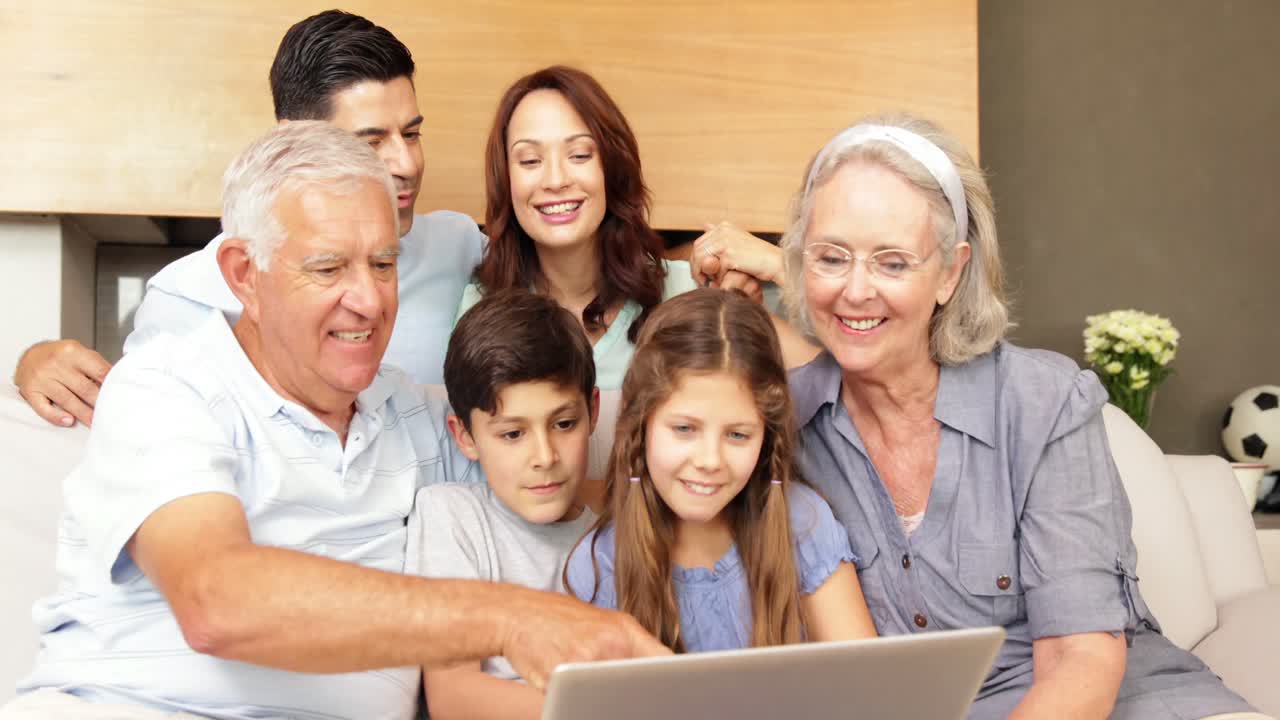 familia extendida feliz usando la computadora portátil juntos en el sofá