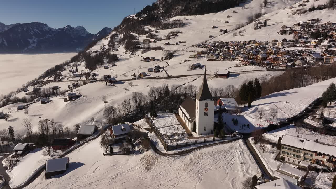 Aerial view of the picturesque village of Amden, Switzerland, blanketed in snow with the iconic St. Gallus Church standing tall.