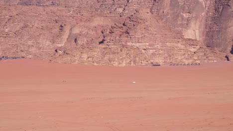 Weißer-Allrad-LKW,-Der-Durch-Die-Weite,-Abgelegene-Wadi-Rum-Wüste-In-Jordanien-Fährt,-Mit-Beduinenzelten,-Die-Sich-An-Berge-In-Der-Ferne-Schmiegen