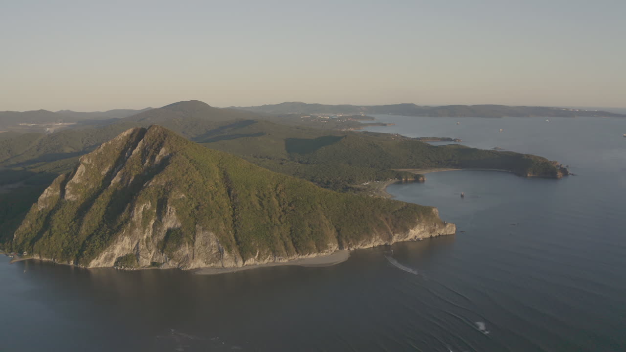 una vista del paisaje de una montaña en forma de pirámide ubicada en el estuario de un río que desemboca en el mar, con vegetación verde en sus lados, una cresta de montaña en el fondo, en la puesta de sol