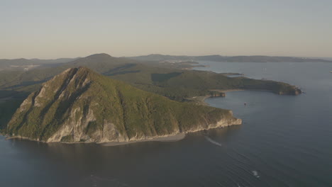 一座位于河口流入海的金字塔形山的景观景观,侧面有绿色植被,背景有山脊,日落