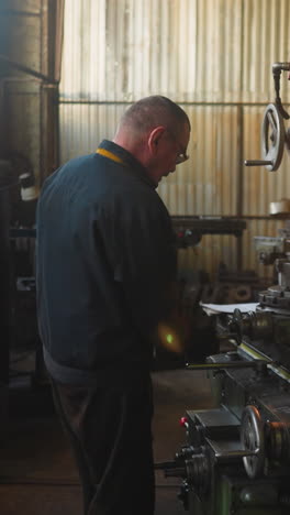 old worker turns valve of milling machine to fix detail in factory workshop. man uses vintage lathe equipment to cut out steel material at plant