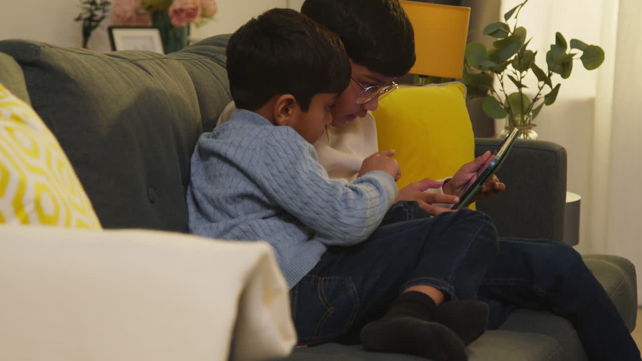 Two Young Boys Sitting On Sofa At Home Playing Games Or Streaming Onto Digital Tablet Together 4