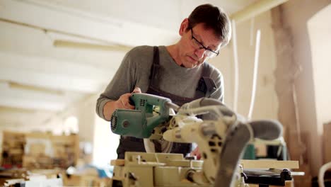 mature carpenter wearing uniform and eyeglasses making cuts in wood with circular saw