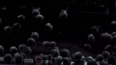 blueberries floating in water against black background in slow motion