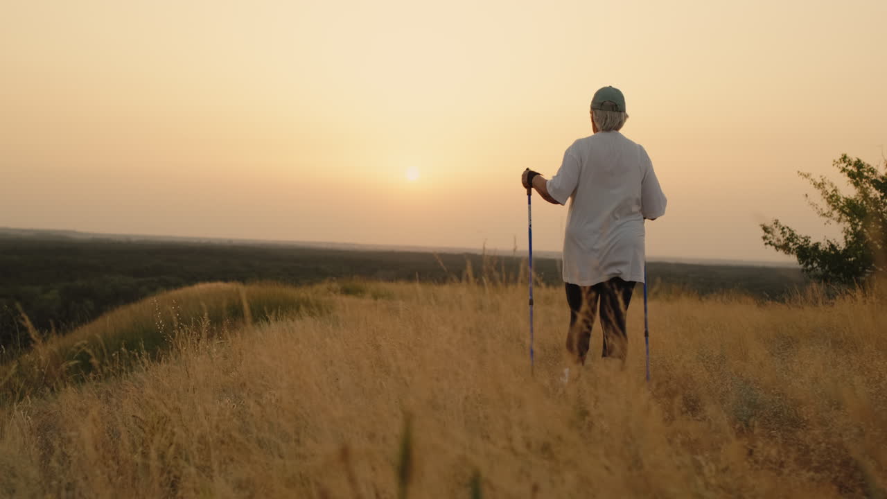 una anciana con bastones nórdicos camina hacia adelante a través de un lugar escénico