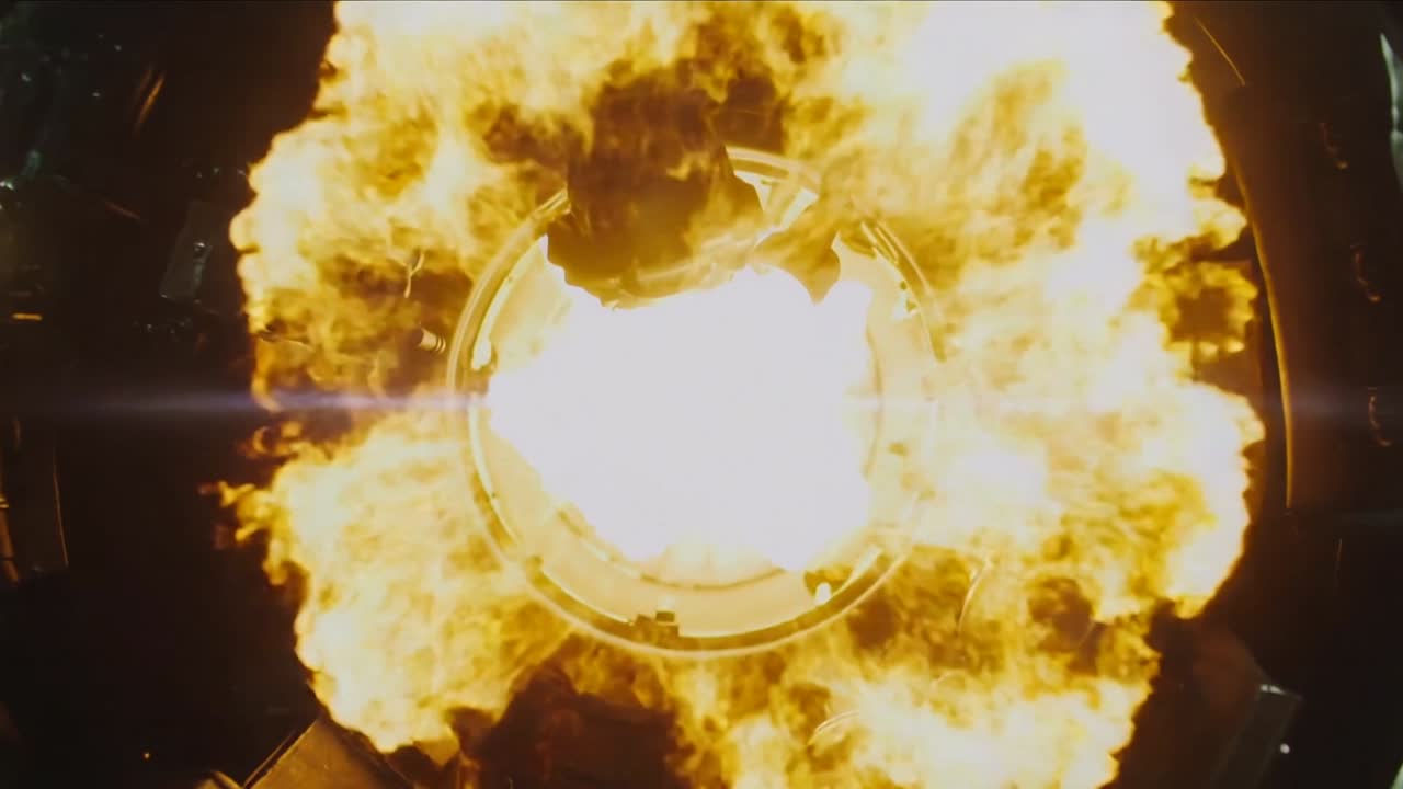 La visiera luminosa di un casco mostra un accenditore che si attiva all'interno di un'astronave, proiettando fiamme e illuminando un guanto di una tuta bianca.