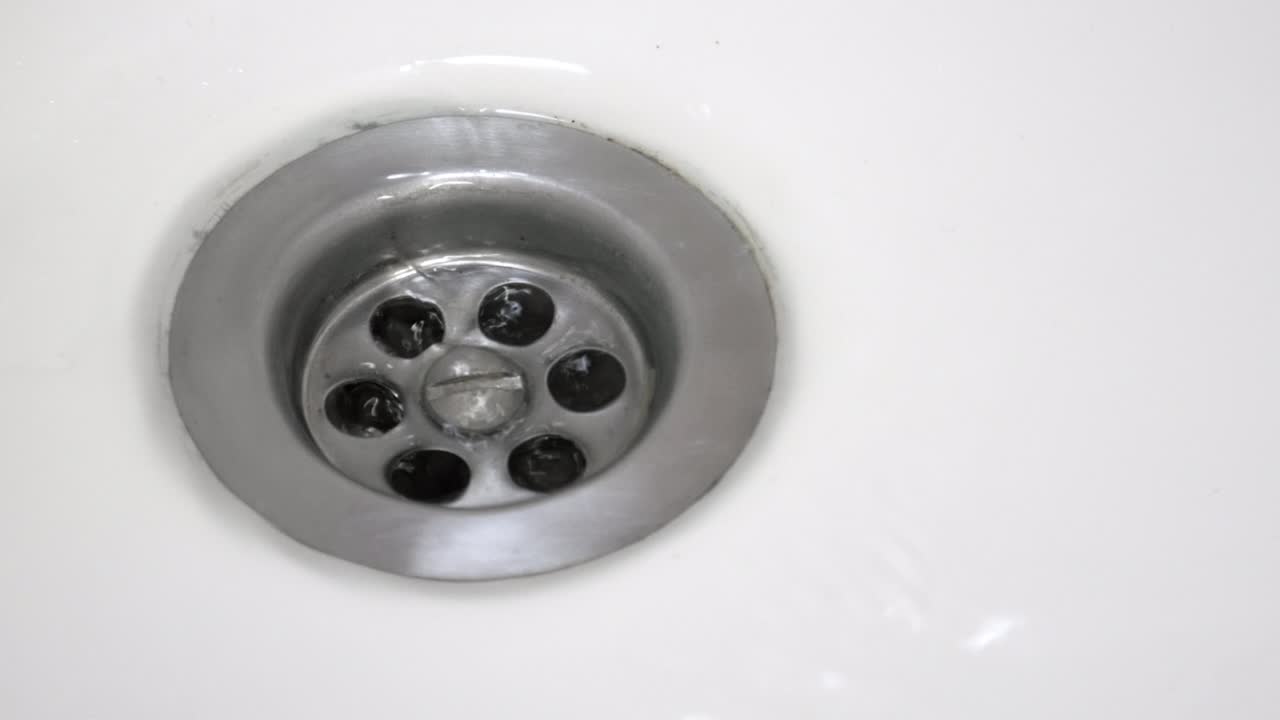 A close-up shot of the water entering the sink drain. 25fps