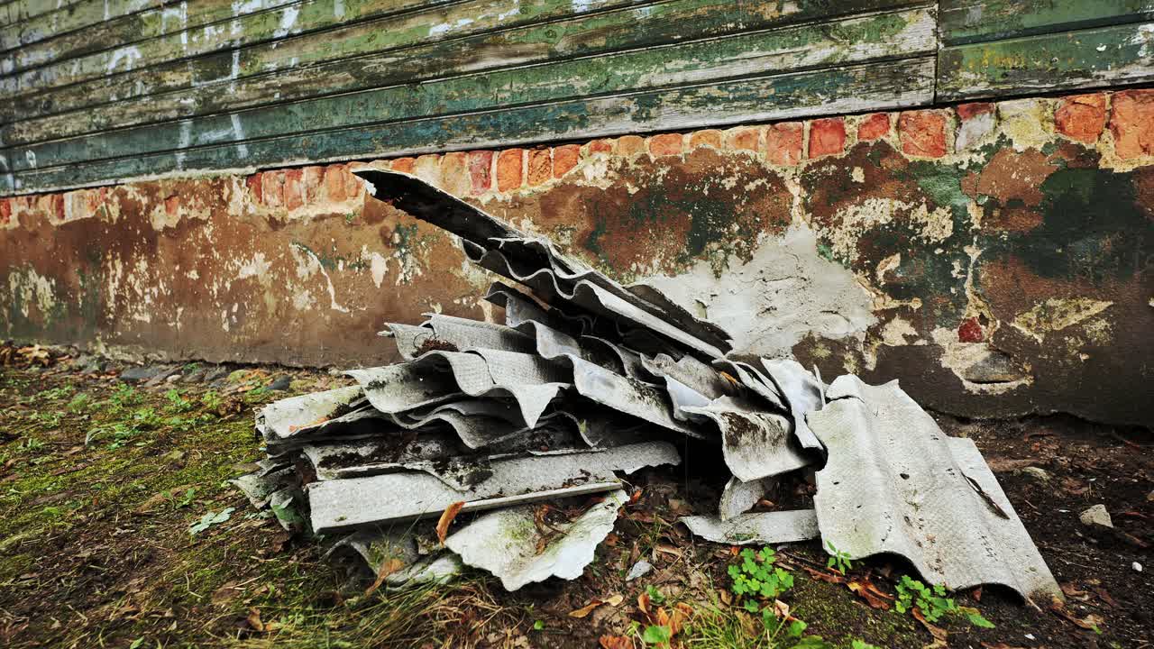 Crumbling asbestos debris leaning against abandoned brick wall in Riga shows urban decay
