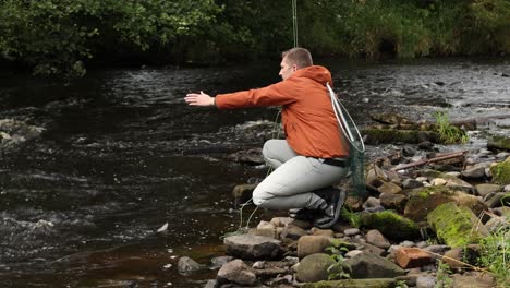 hand-held shot of a flyfisherman reeling in a wild brown trout to release