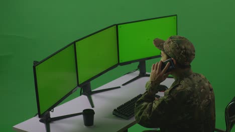 side view of asian man soldier talking on mobile phone while working with mock up multiple computer monitor in green screen studio