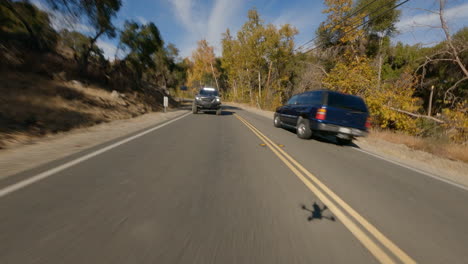 fpv drone shot of black car driving fast on road at morning