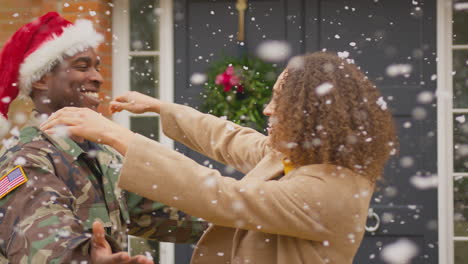 paar mit amerikanischem armee-mann, der einen weihnachtsmannshut trägt, zu hause im urlaub, umarmt vor dem haus zu weihnachten im schnee - in slowmotion gedreht