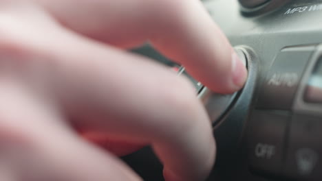 close up finger rotating temperature control dial to increase car air conditioning setting inside cabin with smooth motion focus on metallic knob texture and warm ambient lighting