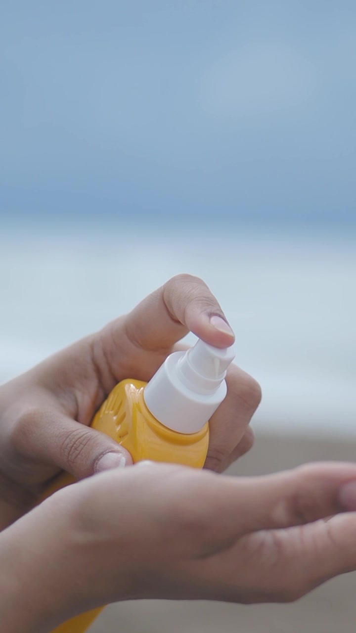 Close-up of Hands Applying Sunscreen Lotion from a Yellow Bottle