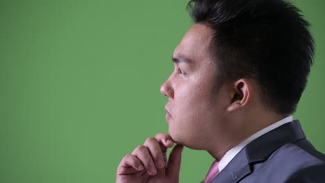 young handsome overweight asian businessman against green background