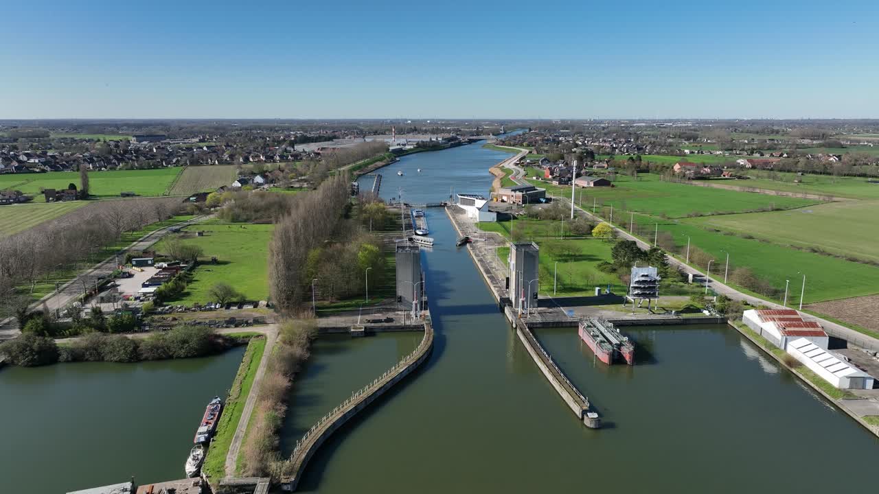 Zoom out aerial shot of Antwerp canal lock with ships navigating through rural countryside, green fields, and small villages under clear sky